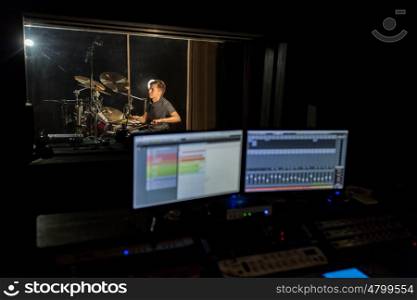 music, people and show business concept - sound mixing console with monitor screens and male musician playing drum kit at recording studio