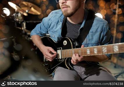 music, people, musical instruments and entertainment concept - close up of male guitarist playing electric guitar at studio rehearsal over holidays lights background. close up of musician playing guitar at studio