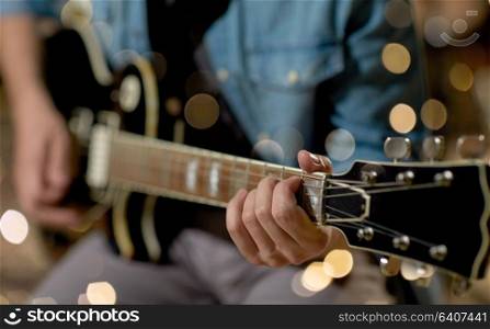 music, people, musical instruments and entertainment concept - close up of male guitarist playing electric guitar at studio rehearsal over festive lights. close up of man playing guitar at studio rehearsal