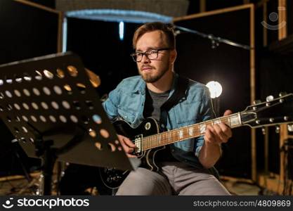 music, people, musical instruments and entertainment concept - male guitarist playing electric guitar with stand at studio rehearsal