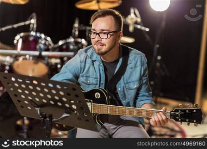 music, people, musical instruments and entertainment concept - male guitarist playing electric guitar with stand at studio rehearsal. man playing guitar at studio rehearsal