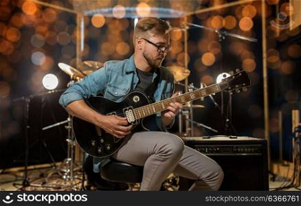 music, people, musical instruments and entertainment concept - male guitarist playing electric guitar at studio or concert over holidays lights background. man playing guitar at studio rehearsal