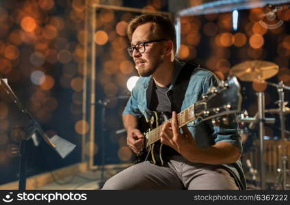 music, people, musical instruments and entertainment concept - male guitarist playing electric guitar with stand at studio or concert over holidays lights background. man playing guitar at studio or concert