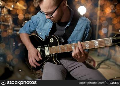 music, people, musical instruments and entertainment concept - male guitarist playing electric guitar at studio or concert over holidays lights background. man playing guitar at studio or concert