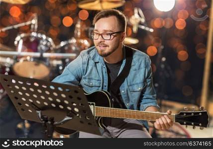 music, people, musical instruments and entertainment concept - male guitarist playing electric guitar with stand at studio rehearsal over holidays lights background. musician playing guitar at studio over lights