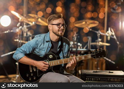 music, people, musical instruments and entertainment concept - male guitarist playing electric guitar at studio rehearsal over holidays lights background. musician playing guitar at studio over lights