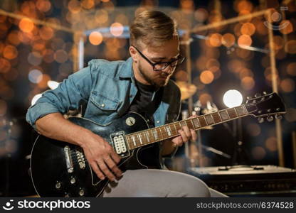 music, people, musical instruments and entertainment concept - male guitarist playing electric guitar at studio rehearsal over holidays lights background. musician playing guitar at studio over lights