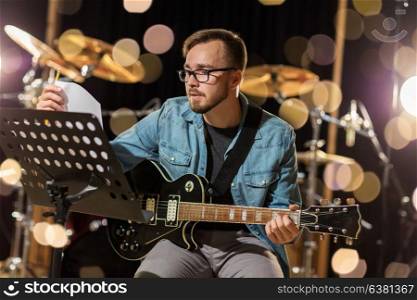 music, people, musical instruments and entertainment concept - male guitarist playing electric guitar with stand at studio rehearsal over lights. man playing guitar at studio rehearsal