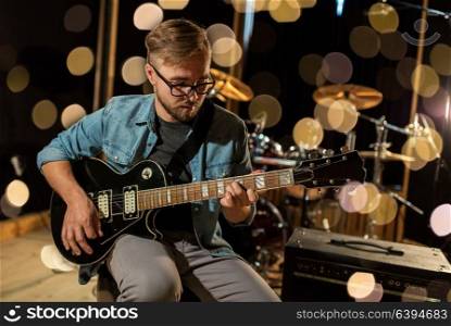 music, people, musical instruments and entertainment concept - male guitarist playing electric guitar at studio rehearsal over lights. man playing guitar at studio rehearsal