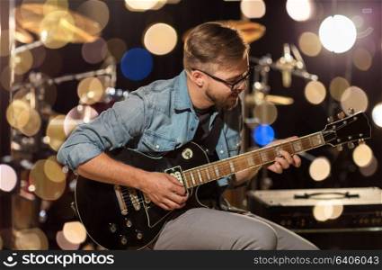 music, people, musical instruments and entertainment concept - male guitarist playing electric guitar at studio rehearsal over festive lights. man playing guitar at studio rehearsal