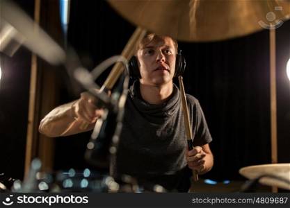 music, people, musical instruments and entertainment concept - male musician in headphones with drumsticks playing drums and cymbals at concert or studio