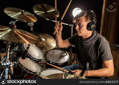 music, people, musical instruments and entertainment concept - male musician in headphones with drumsticks playing drums and cymbals at concert or studio