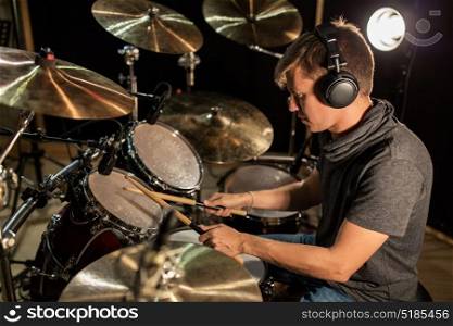 music, people, musical instruments and entertainment concept - male musician in headphones with drumsticks playing drums and cymbals at concert or studio. male musician playing drums and cymbals at concert