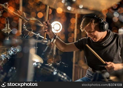 music, people, musical instruments and entertainment concept - male musician in headphones with drumsticks playing drum kit at concert or studio. male musician playing drum kit at concert