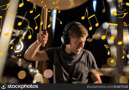 music, people, musical instruments and entertainment concept - male musician in headphones playing drum kit at concert or studio over lights and notes. musician in headphones playing drum kit at concert