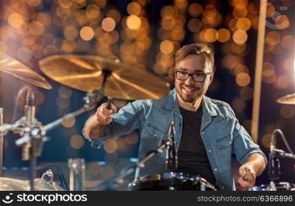music, people, musical instruments and entertainment concept - male musician or drummer playing drums and cymbals at concert or studio over holidays lights background. musician or drummer playing drum kit at concert