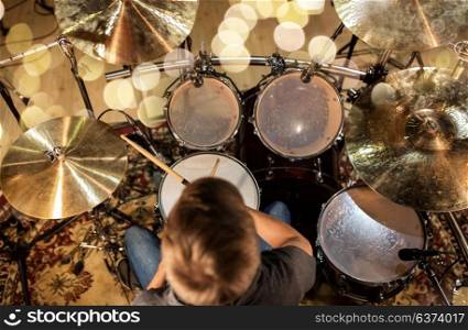 music, people, musical instruments and entertainment concept - male musician or drummer playing drum kit at studio over holidays lights background. musician or drummer playing drum kit at studio