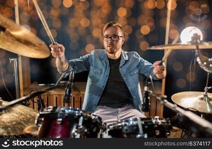 music, people, musical instruments and entertainment concept - male musician or drummer playing drums and cymbals at concert or studio over holidays lights background. musician or drummer playing drum kit at concert