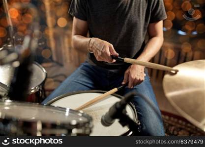 music, people, musical instruments and entertainment concept - male musician or drummer playing drums and cymbals at concert or studio over holidays lights background. musician playing drum kit at concert over lights