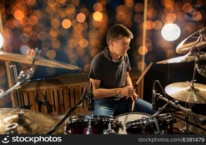 music, people, musical instruments and entertainment concept - male musician or drummer with drumsticks playing drums and cymbals at concert or studio over holidays lights background. musician playing drum kit at concert over lights