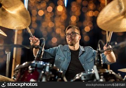 music, people, musical instruments and entertainment concept - male musician or drummer with drumsticks playing drums and cymbals at concert or studio over holidays lights background. musician playing drum kit at concert over lights