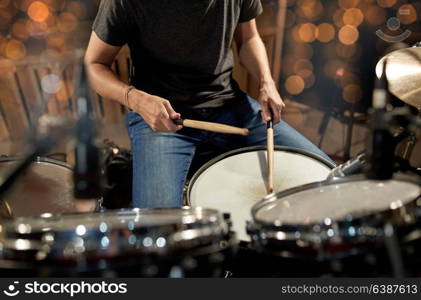 music, people, musical instruments and entertainment concept - male musician or drummer playing drums and cymbals at concert or studio over holidays lights background. musician playing drum kit at concert over lights