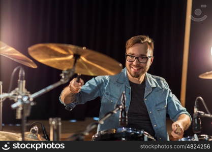 music, people, musical instruments and entertainment concept - male musician with drumsticks playing drums and cymbals at concert or studio