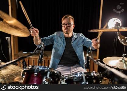 music, people, musical instruments and entertainment concept - male musician with drumsticks playing drums and cymbals at concert or studio