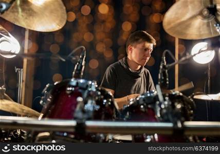 music, people, musical instruments and entertainment concept - male musician with drumsticks playing drum kit at concert or studio over holidays lights background. male musician playing drum kit at concert