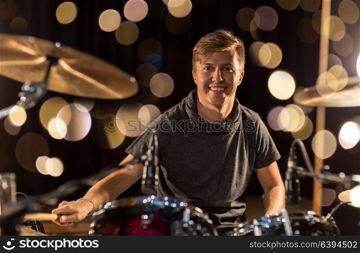 music, people, musical instruments and entertainment concept - male musician with drumsticks playing drum kit at concert or studio over lights. male musician playing drum kit at concert