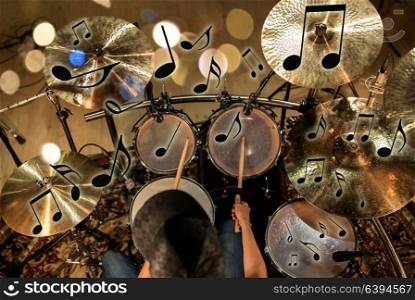music, people, musical instruments and entertainment concept - male musician with drumsticks playing drum kit at concert or studio over lights and notes. male musician playing drum kit at concert