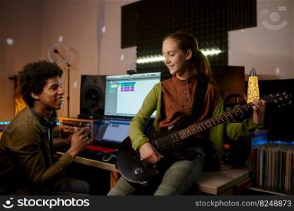 Music producer and teenager girl guitarist at mixing console creating hit song track in recording studio. Music producer and teenager girl guitarist at recording studio