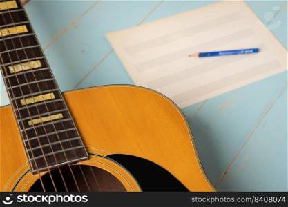 Music recording scene with guitar, empty music sheet and pencil on wooden table