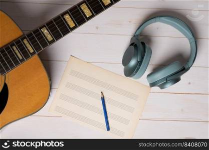 Music recording scene with guitar, empty music sheet, pencil and headphones on white wooden table