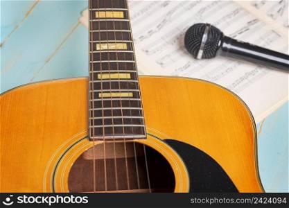 Music recording scene with guitar, music sheets and black microphone on wooden table, closeup