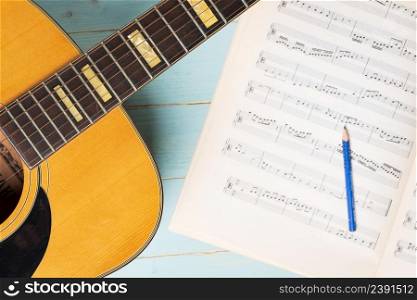Music recording scene with guitar, music sheets and pencil on wooden table, closeup
