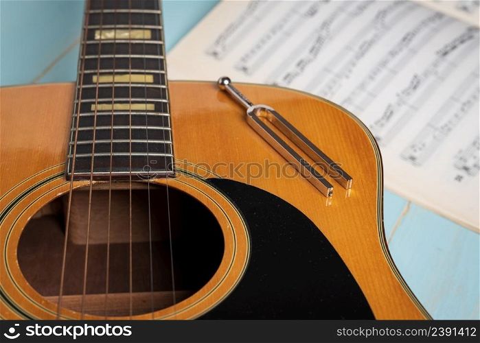 Music recording scene with guitar, music sheets and tuning fork on wooden table, closeup