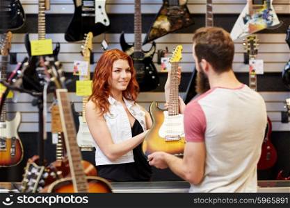 music, sale, people, musical instruments and entertainment concept - female assistant showing electric guitar to customer at music store