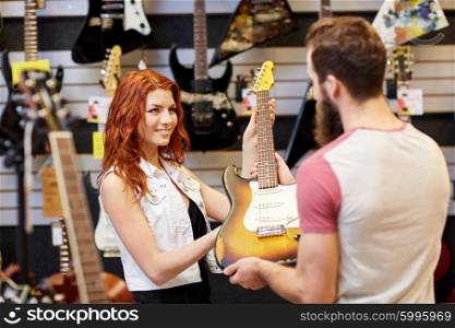 music, sale, people, musical instruments and entertainment concept - female assistant showing electric guitar to customer at music store