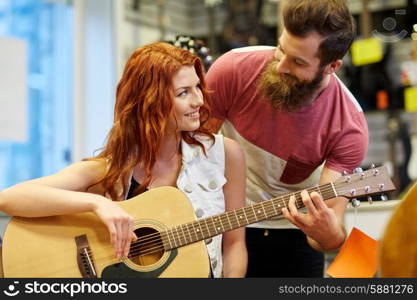 music, sale, people, musical instruments and entertainment concept - happy couple of musicians with guitar at music store