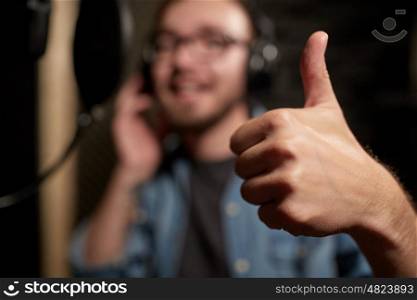 music, show business, people and voice concept - hand of singer showing thumbs up at sound recording studio