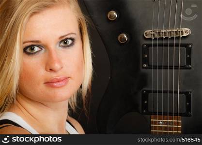 Music, singing concept. Blonde musically talented woman holding electric guitar on black background. Blonde woman holding electric guitar, black background