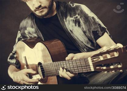 Music, sound, passion concept. Man playing on acoustic guitar, studio shot, black background, sepia vintage colors. Closeup of man playing acoustic guitar