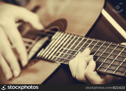 Music, sound, passion concept. Man playing on acoustic guitar, studio shot, black background, sepia vintage colors. Closeup of man playing acoustic guitar