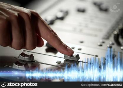 music, technology and equipment concept - male hand moving switch on mixing console in sound recording studio. hand using mixing console for music recording