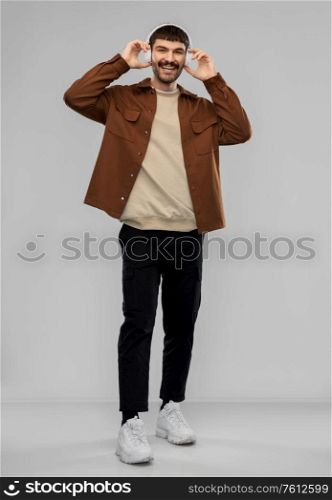 music, technology and people concept - happy smiling young man in headphones over grey background. happy smiling young man in headphones