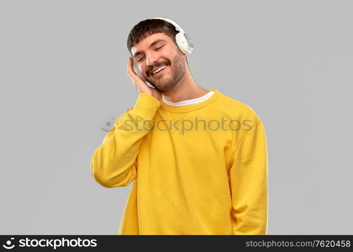 music, technology and people concept - happy smiling young man in headphones over grey background. happy young man in headphones listening to music