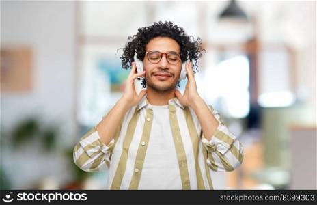 music, technology and people concept - happy smiling young man in headphones over office background. happy smiling young man in headphones at office
