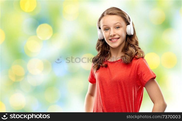 music, technology and people concept - happy teenage girl in headphones and red t-shirt over summer green lights background. happy teenage girl in headphones over green lights