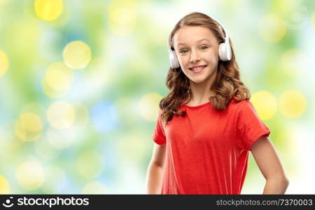 music, technology and people concept - happy teenage girl in headphones and red t-shirt over summer green lights background. happy teenage girl in headphones over green lights